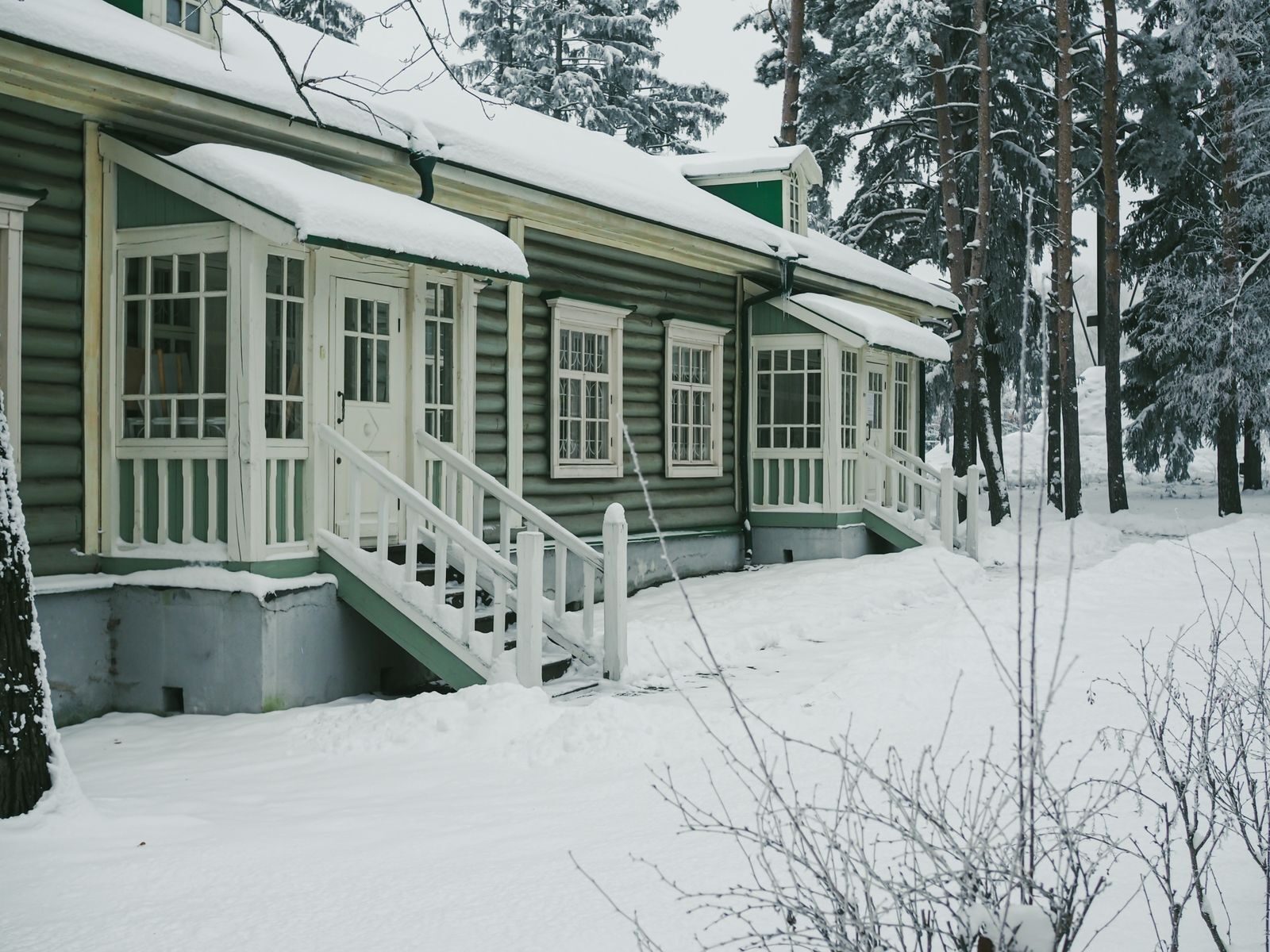 Lumipeitteinen vanha puutalo mäntyjen keskellä