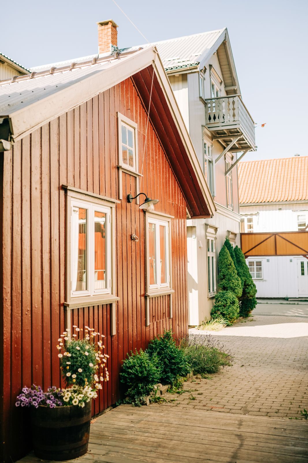 Punainen puutalo ja kukkaistutuksia aurinkoisella pihalla.