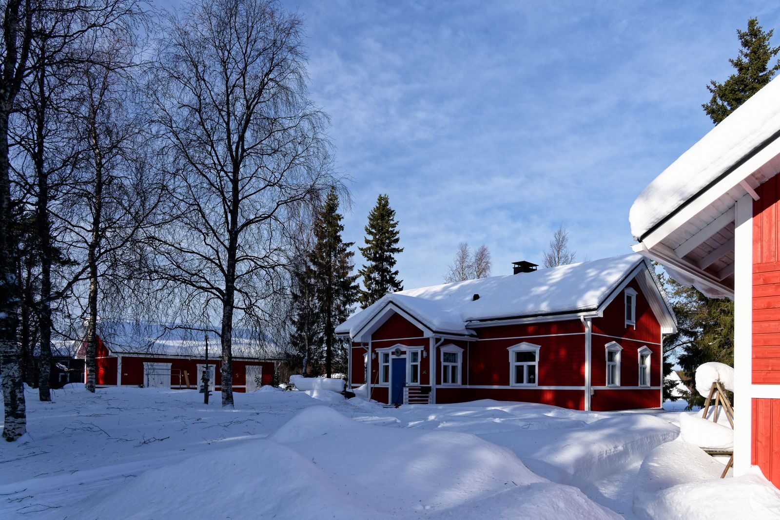 Punainen puutalo lumisella pihalla talvella.