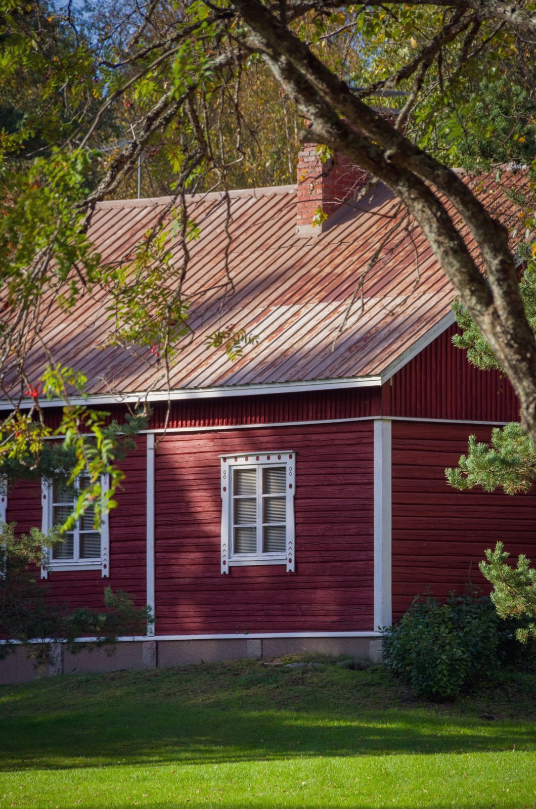 Punainen puutalo vihreän pihan reunalla
