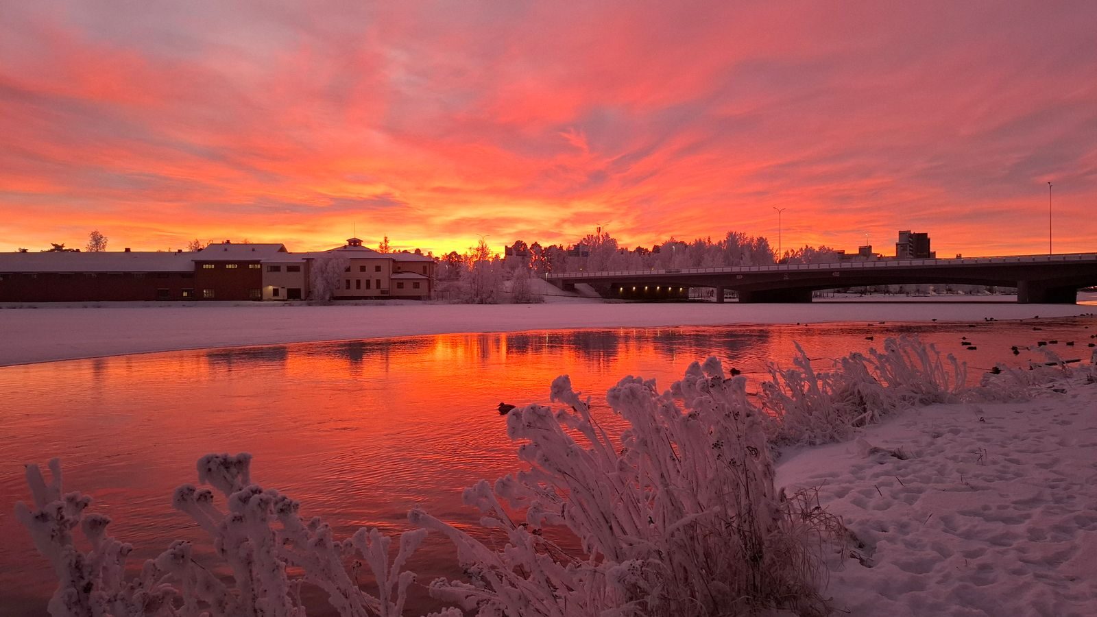 Talvinen jokimaisema ja rakennuksia auringonlaskussa, kuvituskuva sähkösopimuksesta