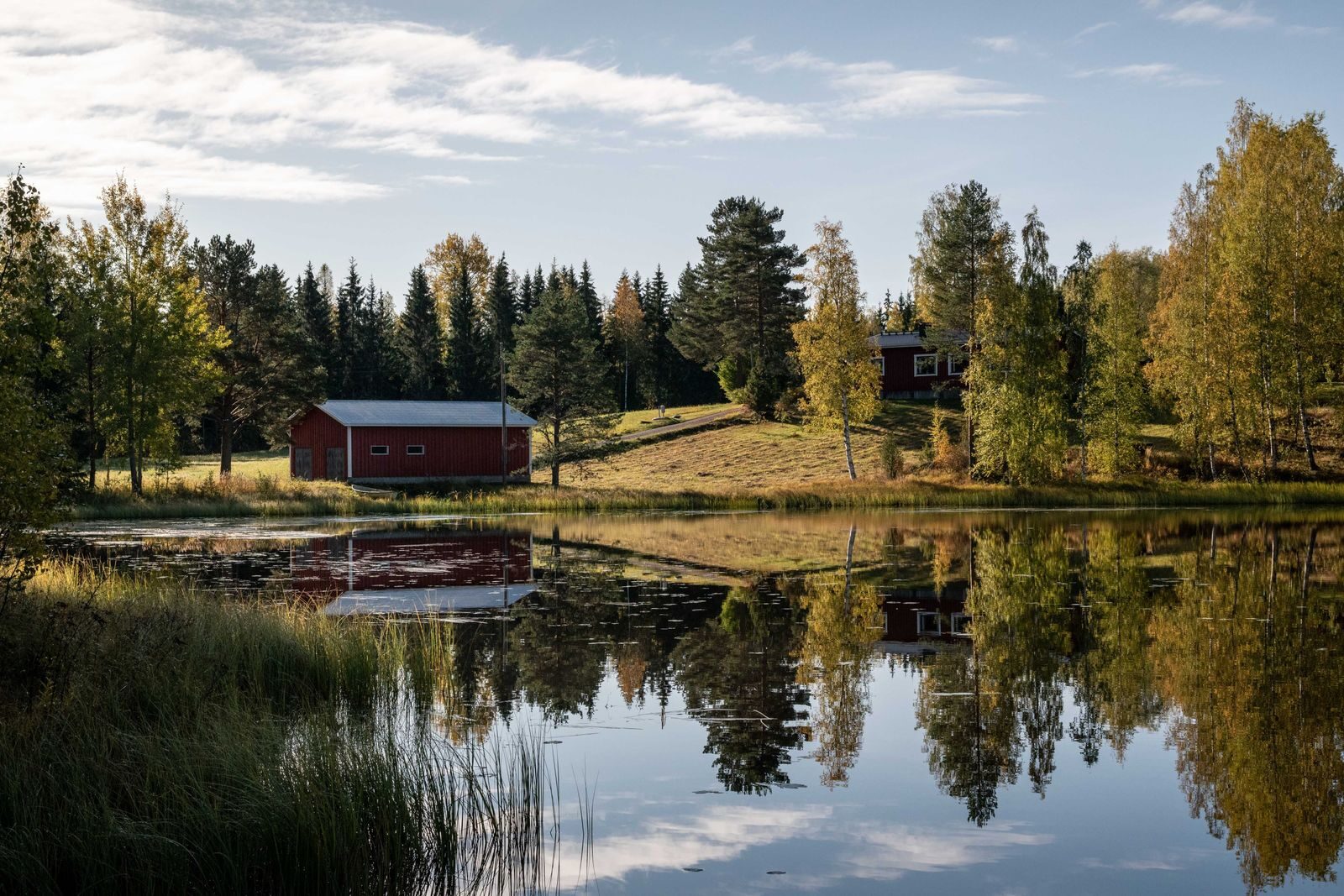 Järven rannalla sijaitseva punainen rakennus ja puiden heijastus vedessä
