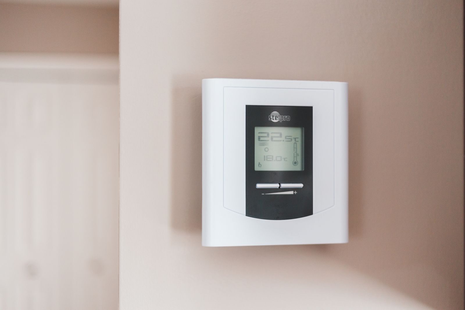 Valkoinen digitaalinen termostaatti seinällä.
