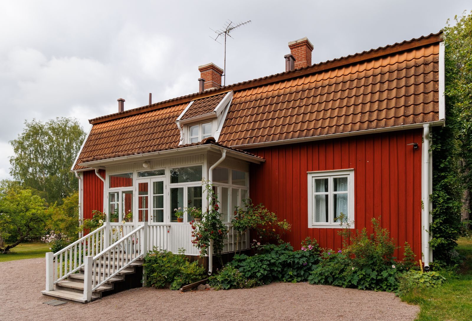 Punainen puutalo, valkoinen lasikuisti ja vehreä piha.