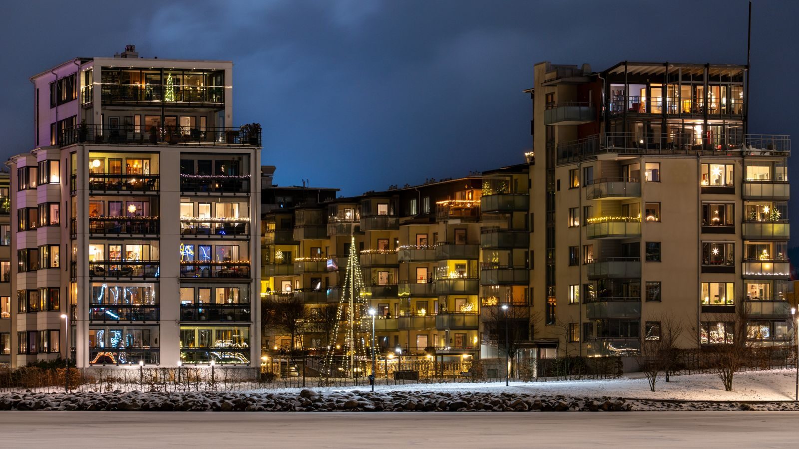 Kerrostalojen valaistuja ikkunoita ja luminen piha talvi-iltana.