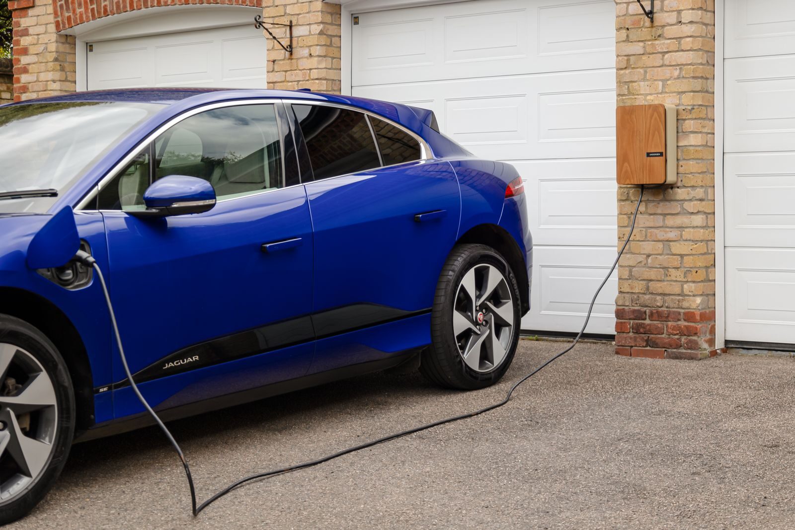 Sininen sähköauto latauksessa autotallin seinään kiinnitetyllä latauslaitteella.