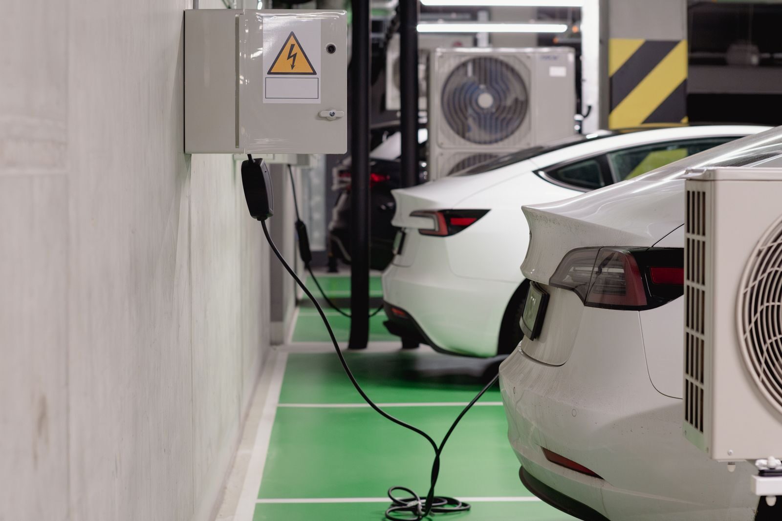 Sähköautoja latauksessa pysäköintihallin seinään asennetuilla latauslaitteilla.