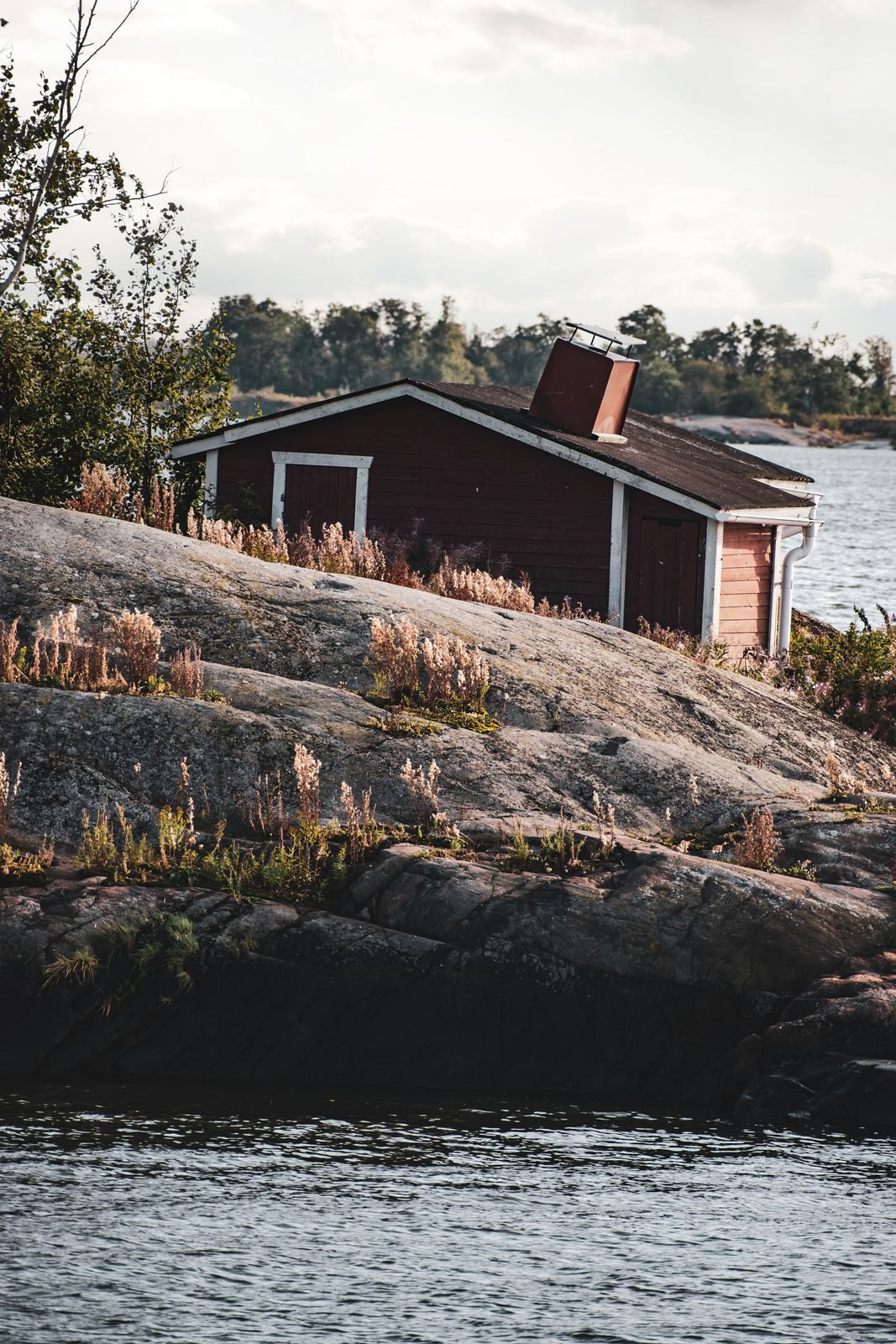Punainen puumökki kallioisella rannalla veden äärellä.