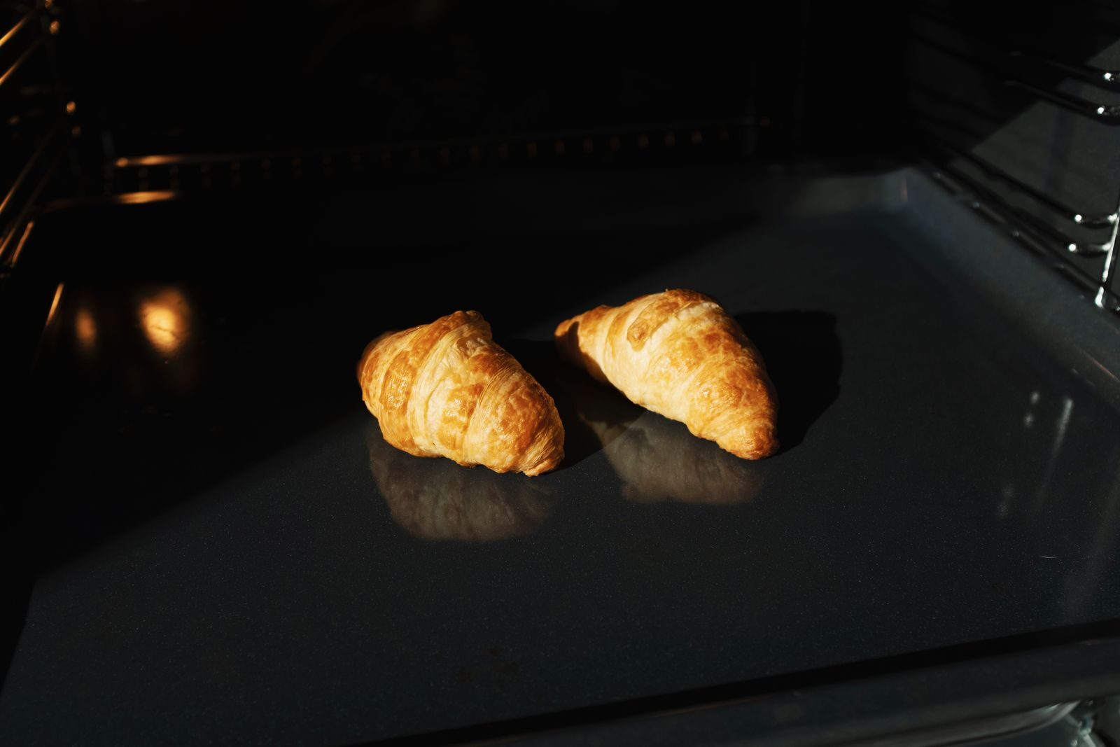 Kaksi croissanttia paistumassa uunin pellillä.