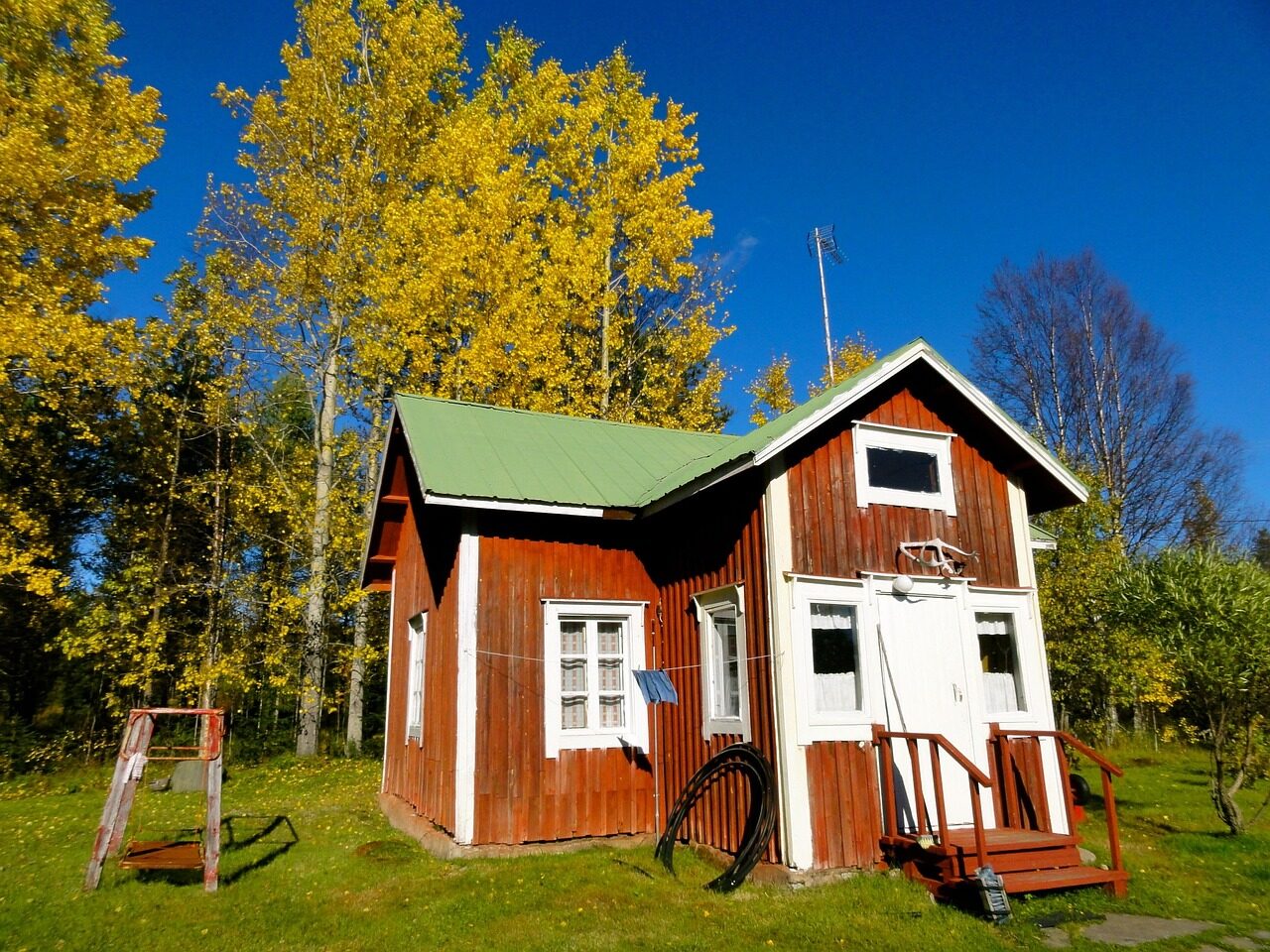 Punainen puumökki ja keltaisia koivuja aurinkoisena syyspäivänä.