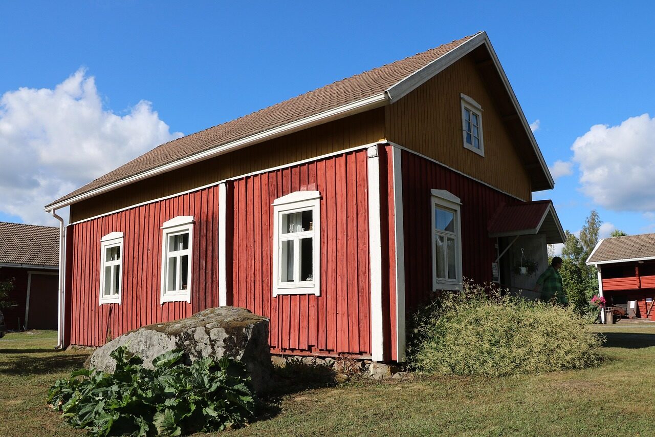 Punainen puutalo valkoisine ikkunanpielineen ja nurmikkopiha.